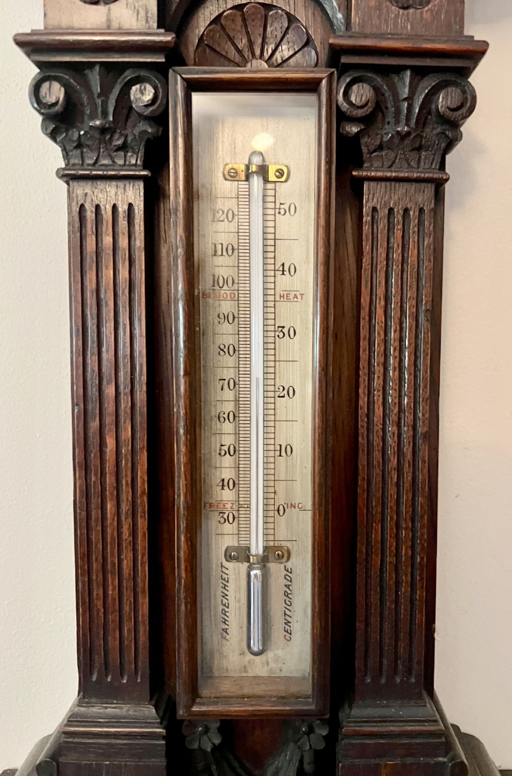 A Victorian carved dark oak wall barometer featuring an upper mercury thermometer flanked by fluted columns and a lower circular brass-rimmed aneroid dial. View III