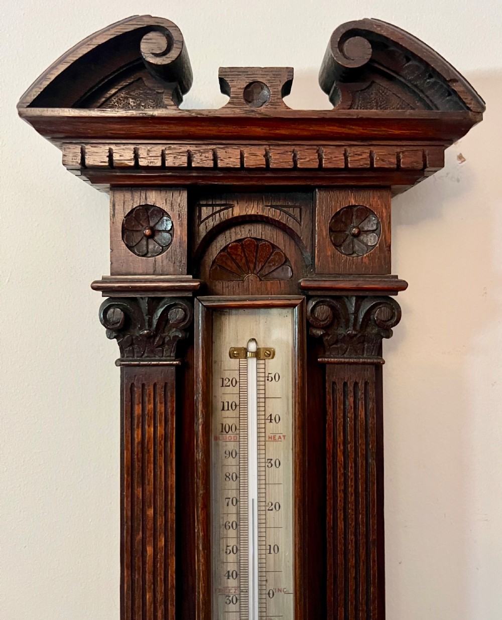 A Victorian carved dark oak wall barometer featuring an upper mercury thermometer flanked by fluted columns and a lower circular brass-rimmed aneroid dial. View IV