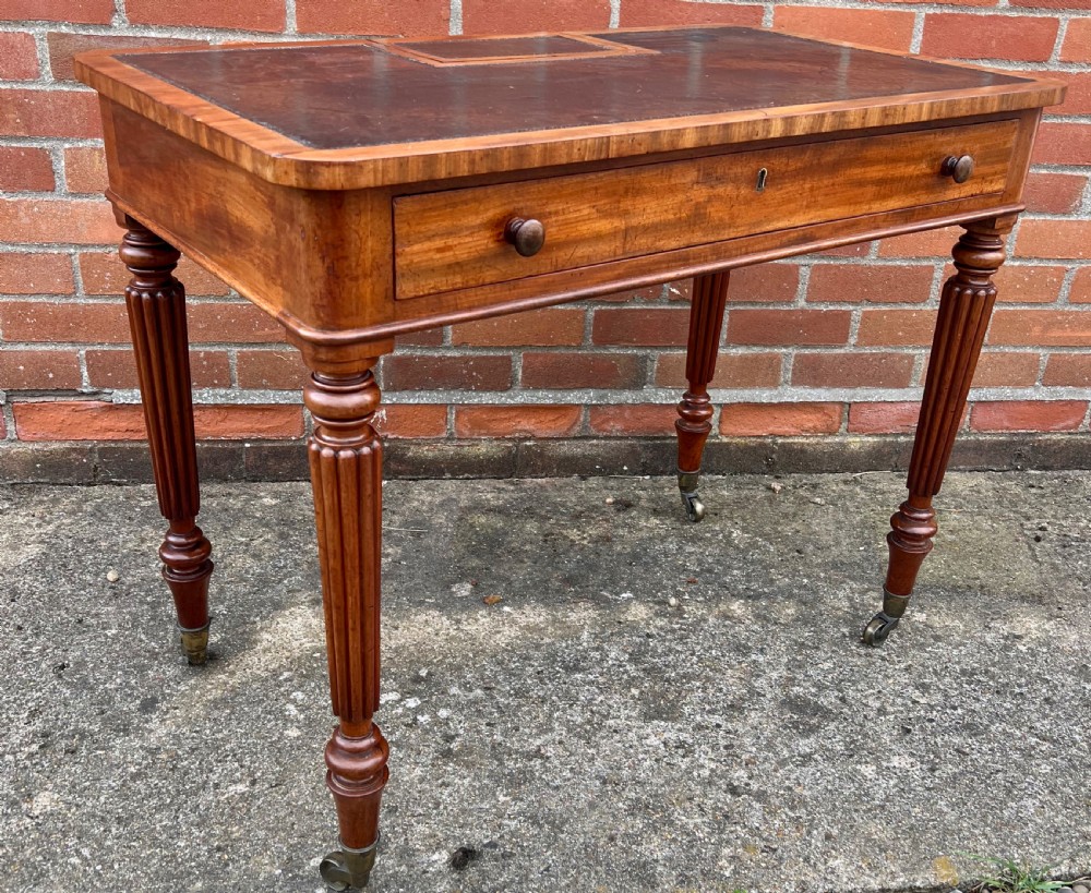 A Regency mahogany chamber writing table featuring a leather-inset surface, single long drawer, turned wooden knobs, and reeded legs on brass castors.