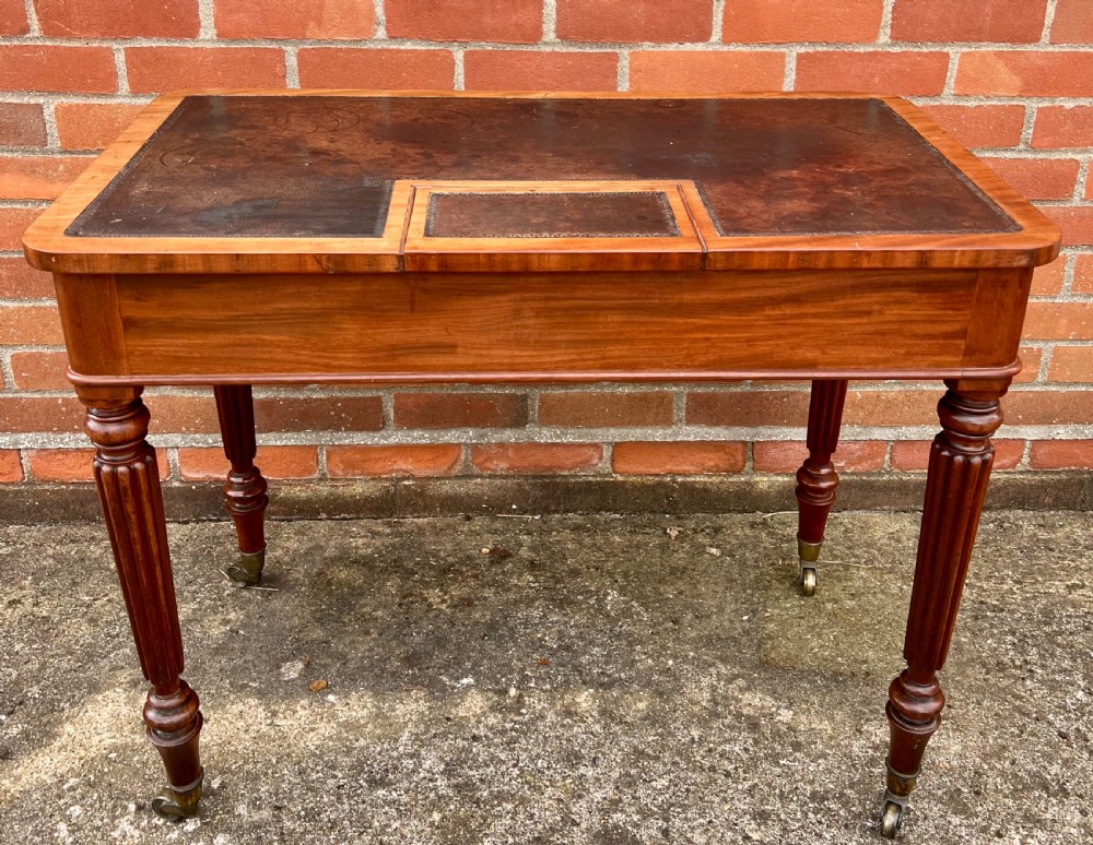 A Regency mahogany chamber writing table featuring a leather-inset surface, single long drawer, turned wooden knobs, and reeded legs on brass castors. View IV