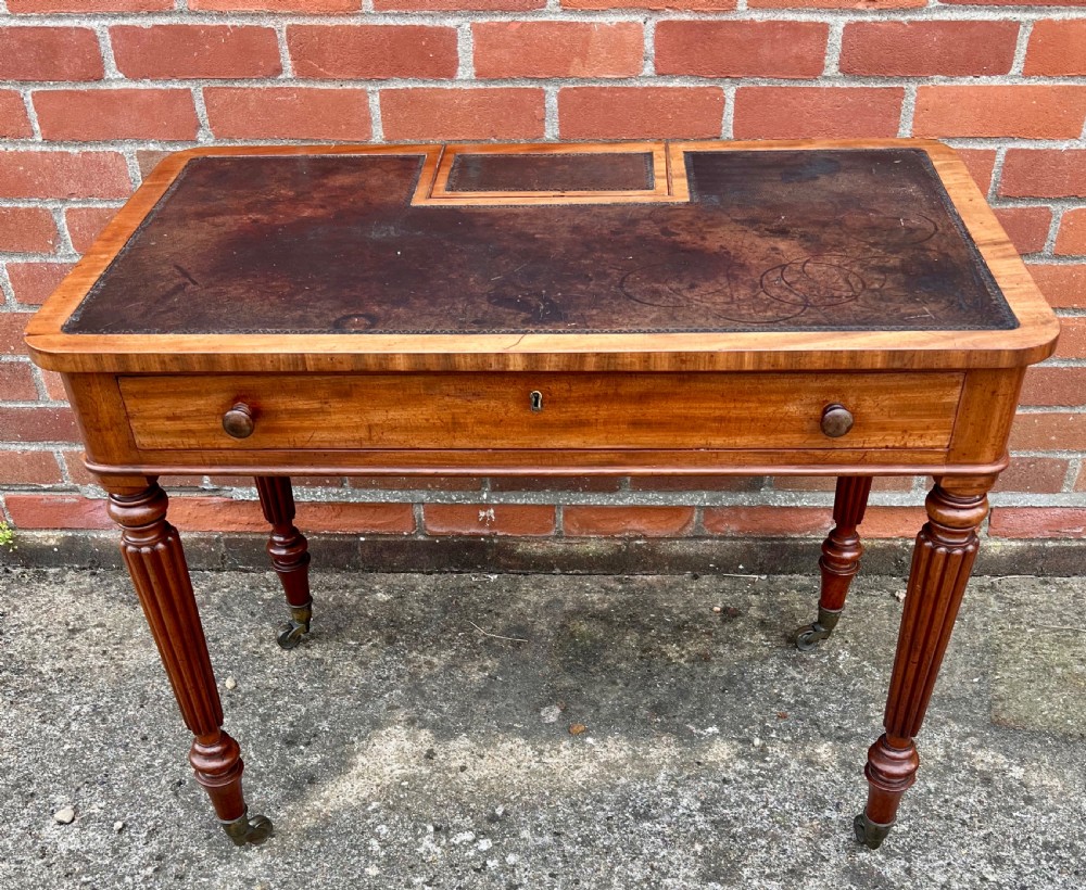 A Regency mahogany chamber writing table featuring a leather-inset surface, single long drawer, turned wooden knobs, and reeded legs on brass castors. View VI