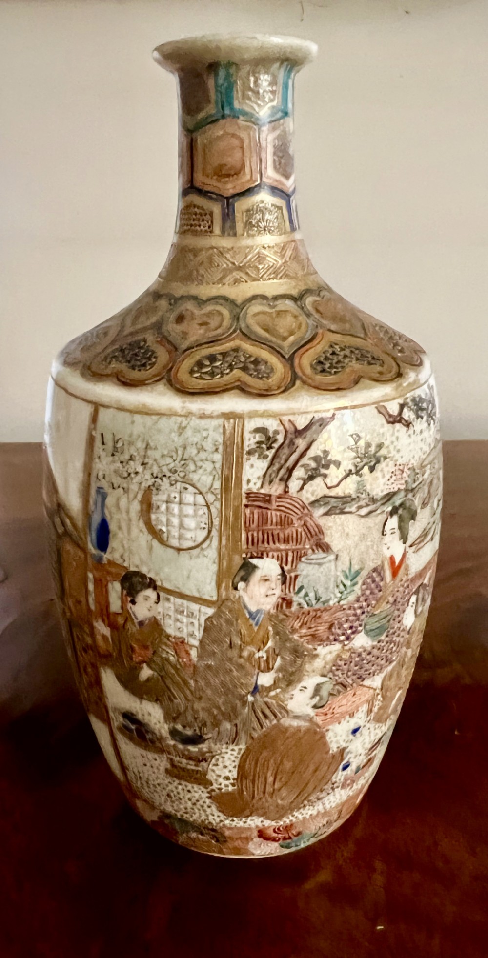 A small Japanese Satsuma earthenware vase featuring a cream crackle glaze, hand-painted figural scenes, and gilded geometric neck detailing.