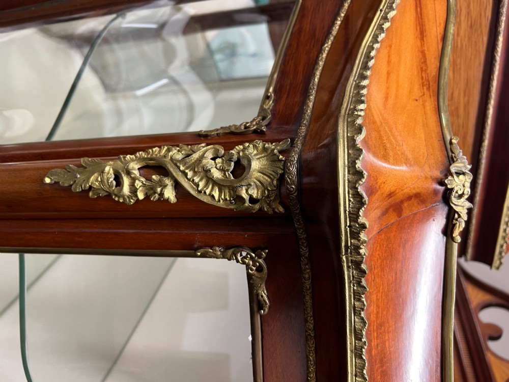An antique French Louis XV style vitrine cabinet featuring a serpentine glass front, gilded ormolu mounts, parquetry lower panels, and cabriole legs. View V