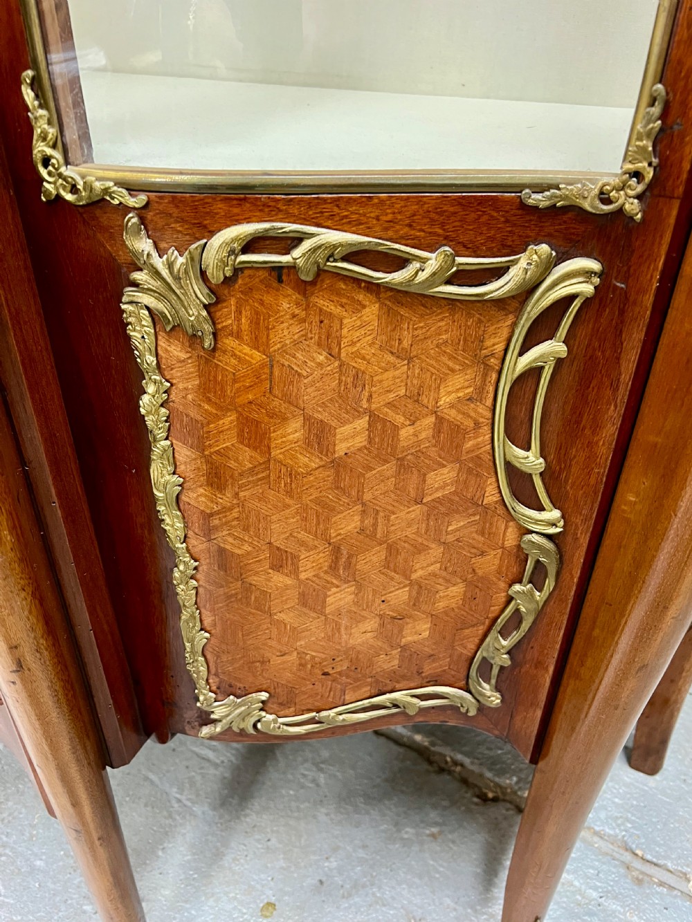 An antique French Louis XV style vitrine cabinet featuring a serpentine glass front, gilded ormolu mounts, parquetry lower panels, and cabriole legs. View VIII