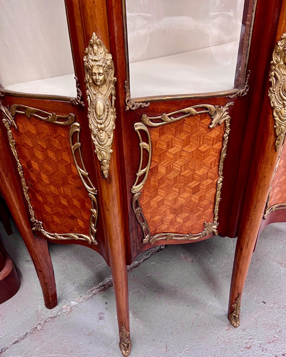 An antique French Louis XV style vitrine cabinet featuring a serpentine glass front, gilded ormolu mounts, parquetry lower panels, and cabriole legs. View X