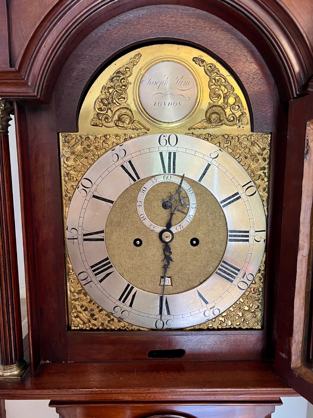 A George III mahogany longcase clock featuring an inlaid trunk door, brass eagle finials, fluted columns, and a brass dial with silvered chapter ring. View II