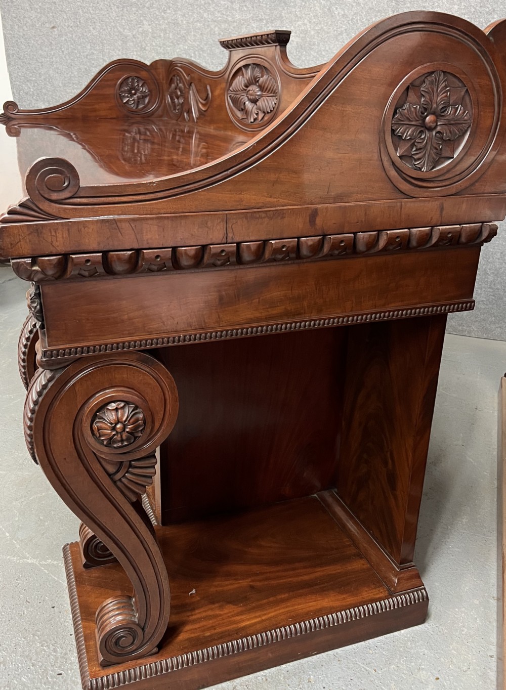 A large Regency mahogany sideboard featuring carved floral scrolls on the raised backboard, heavy carved scroll supports, and panelled cupboard doors. View III