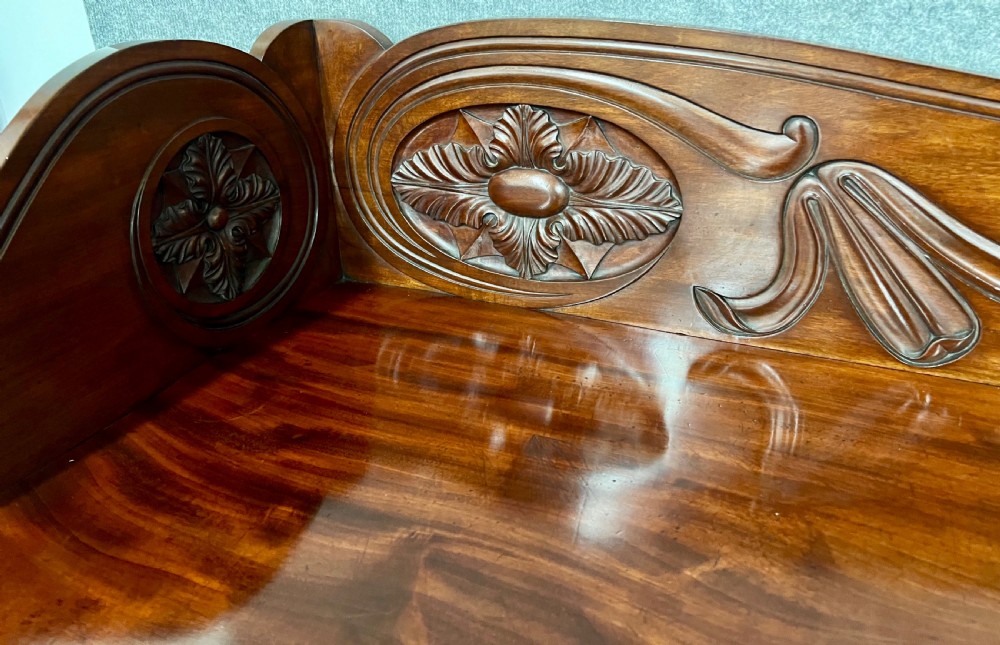 A large Regency mahogany sideboard featuring carved floral scrolls on the raised backboard, heavy carved scroll supports, and panelled cupboard doors. View V