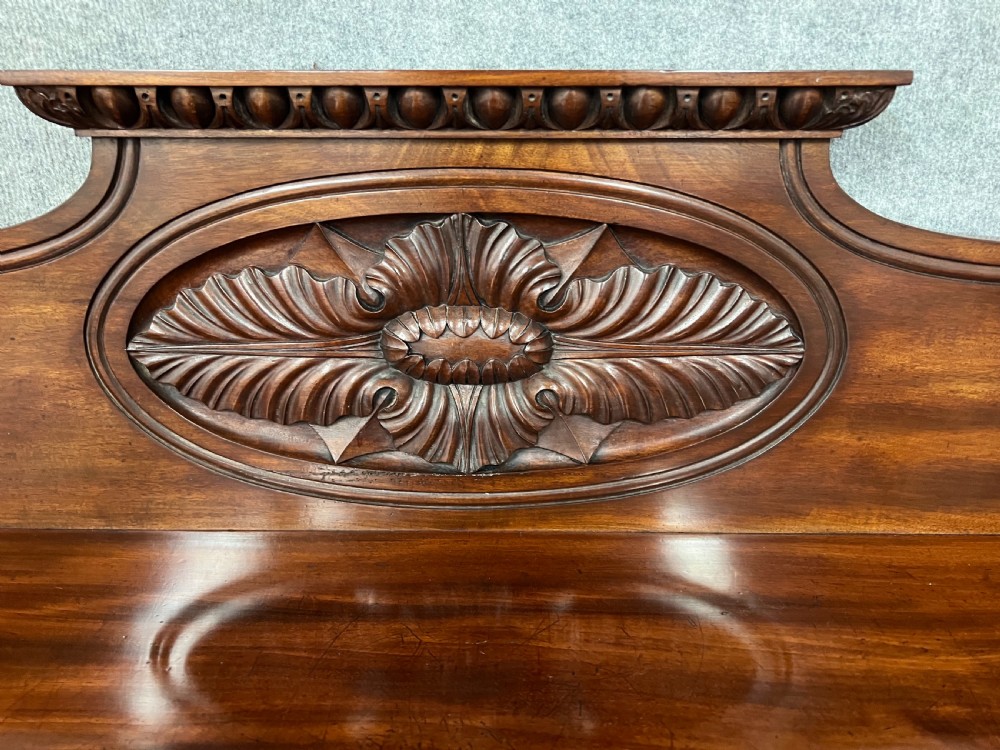 A large Regency mahogany sideboard featuring carved floral scrolls on the raised backboard, heavy carved scroll supports, and panelled cupboard doors. View VII
