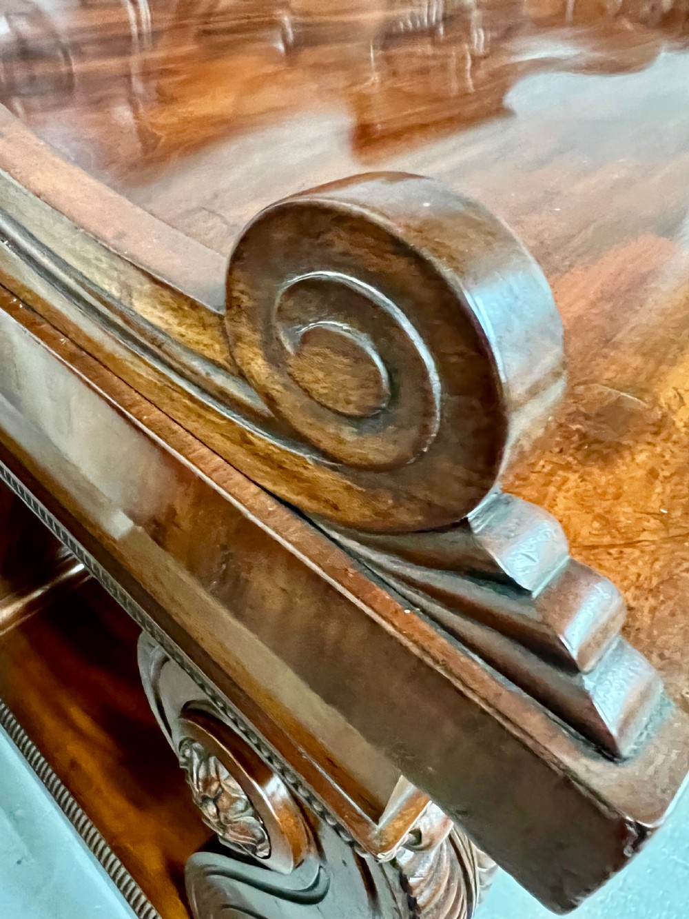 A large Regency mahogany sideboard featuring carved floral scrolls on the raised backboard, heavy carved scroll supports, and panelled cupboard doors. View IX