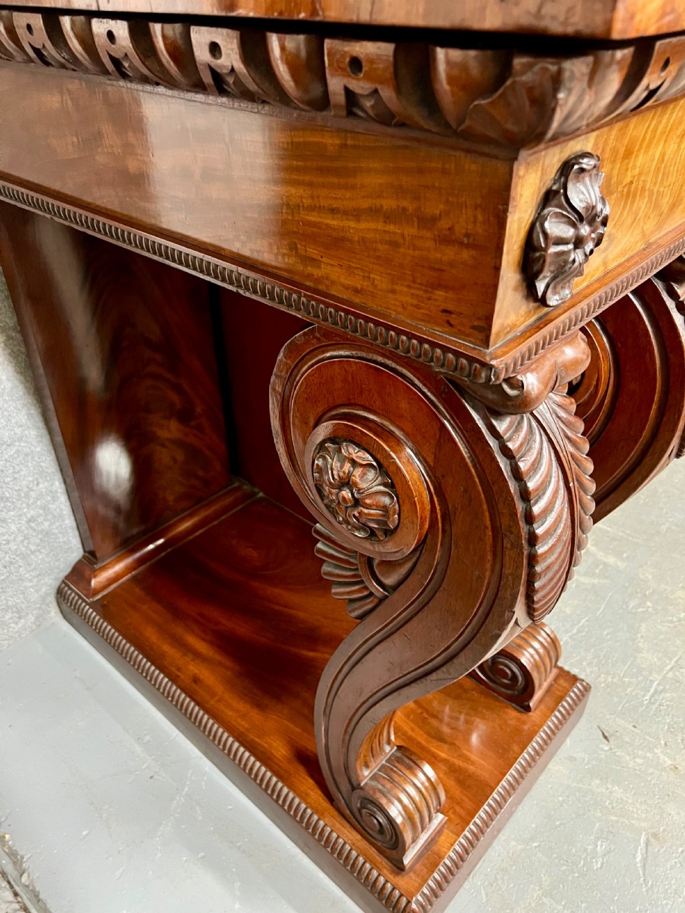 A large Regency mahogany sideboard featuring carved floral scrolls on the raised backboard, heavy carved scroll supports, and panelled cupboard doors. View XI
