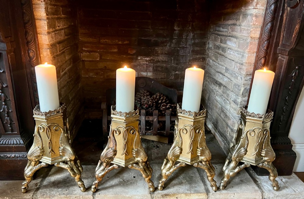 A set of four large ornate cast brass candlesticks featuring pierced crenellated rims, square pedestal bases, and sculpted winged legs ending in hoof feet. View IV
