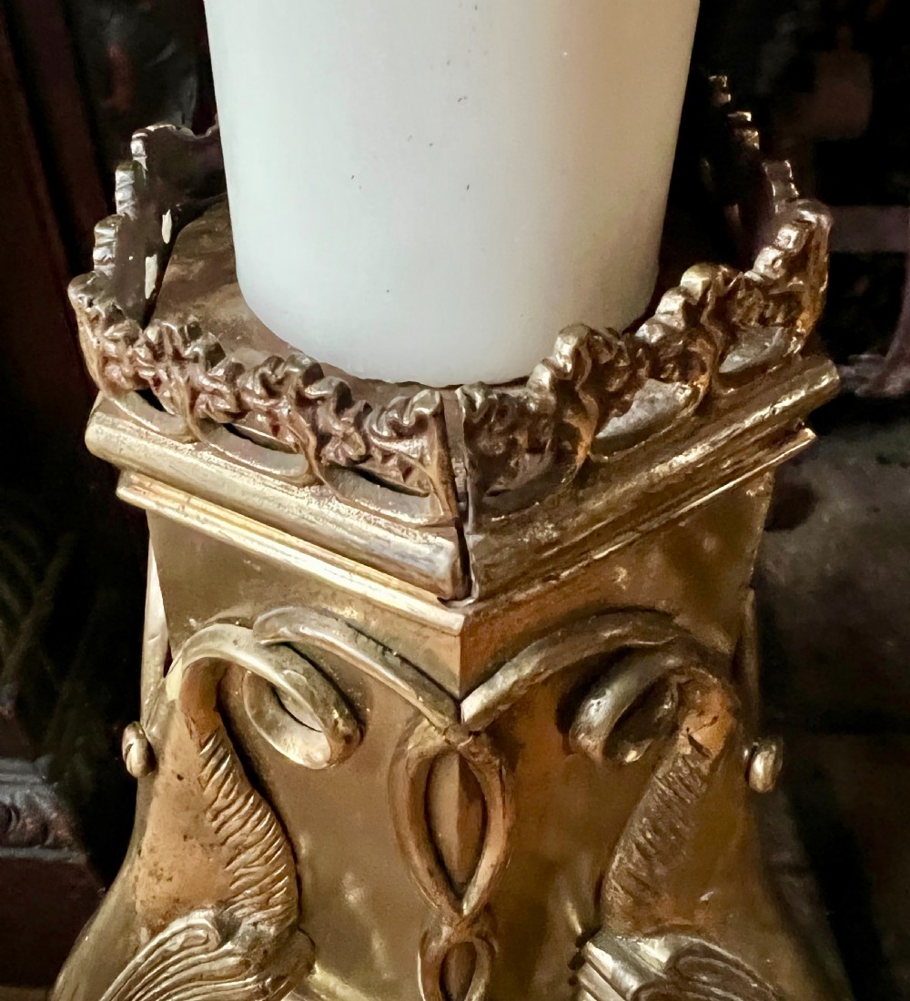 A set of four large ornate cast brass candlesticks featuring pierced crenellated rims, square pedestal bases, and sculpted winged legs ending in hoof feet. View VI