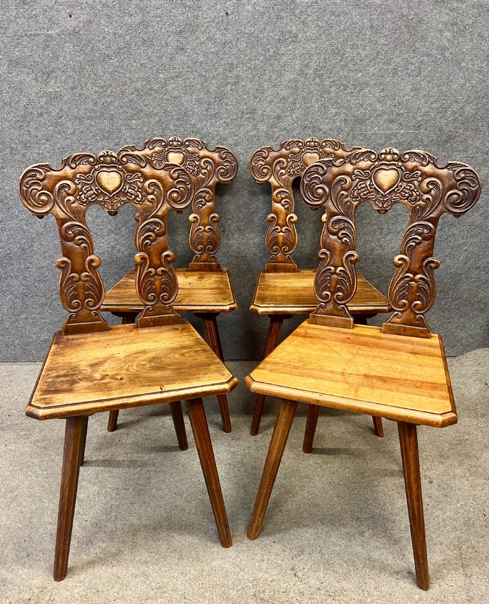 A set of four carved timber Swiss Alpine escabelle chairs featuring detailed scrollwork and heart motifs on the backrests with splayed tapered legs.