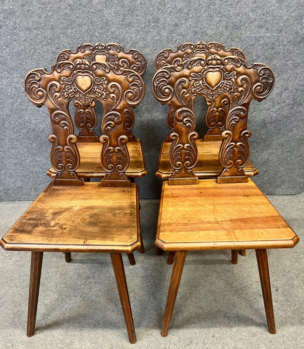 A set of four carved timber Swiss Alpine escabelle chairs featuring detailed scrollwork and heart motifs on the backrests with splayed tapered legs. View II