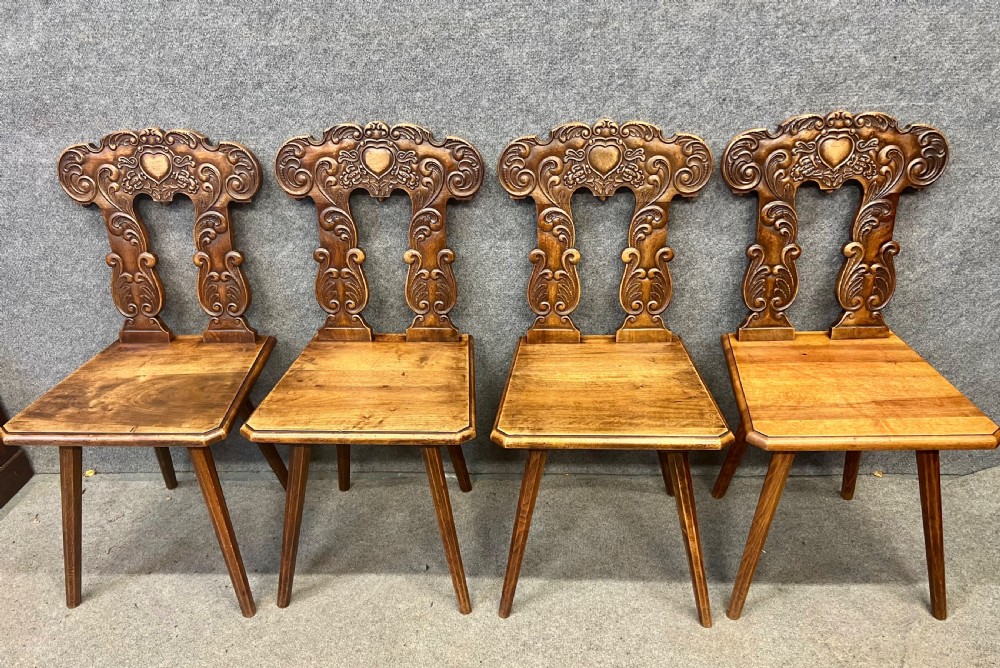 A set of four carved timber Swiss Alpine escabelle chairs featuring detailed scrollwork and heart motifs on the backrests with splayed tapered legs. View III