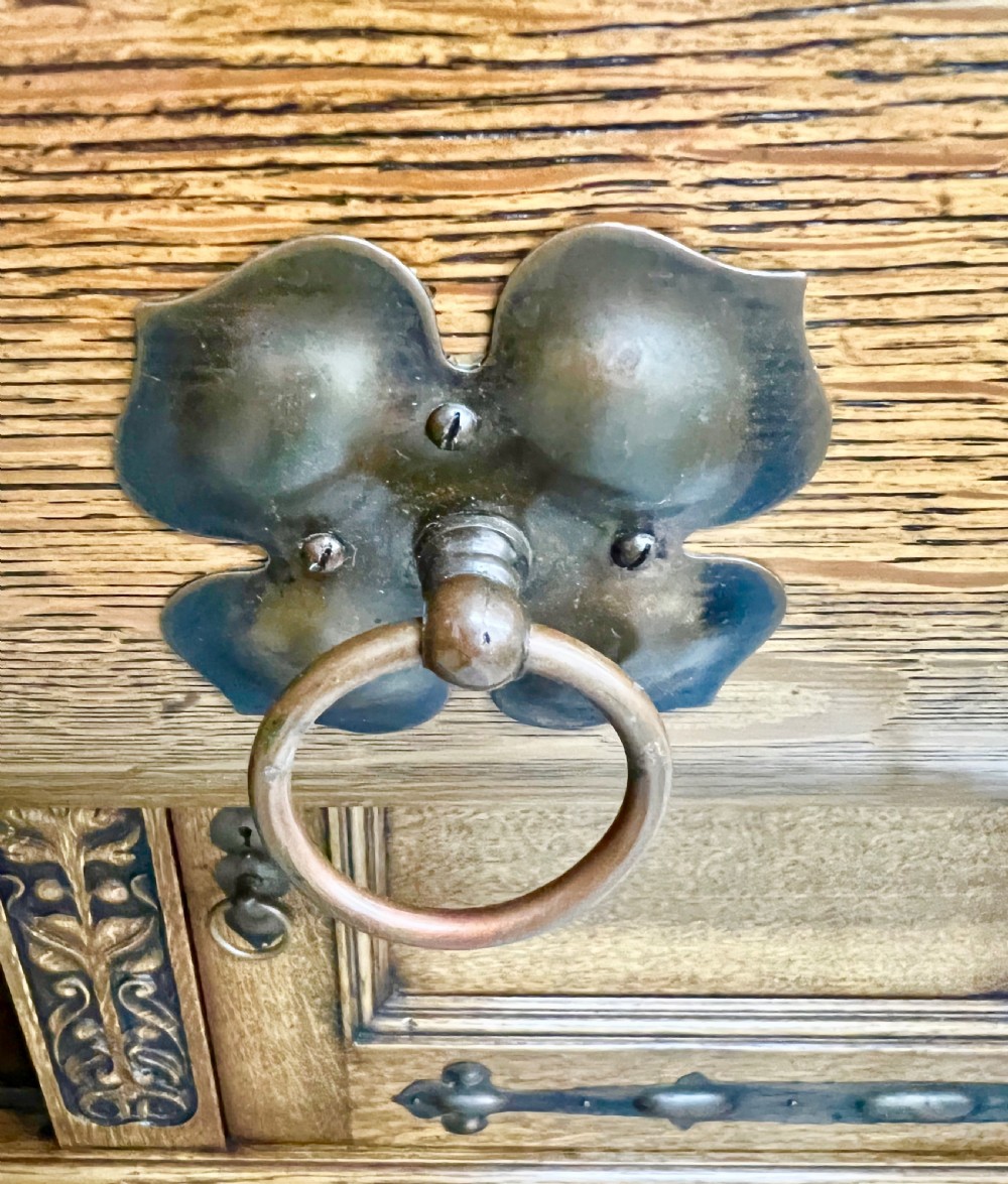 A golden oak Arts and Crafts sideboard featuring an upper shelf, a central repousse copper relief panel above two mirrors, and a lower cabinet with iron strap hinges and carved details. View VIII