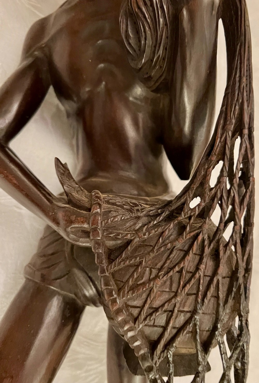 A hand-carved dark hardwood sculpture of a Chinese fisherman holding a net and basket on a stylised wave base. View III