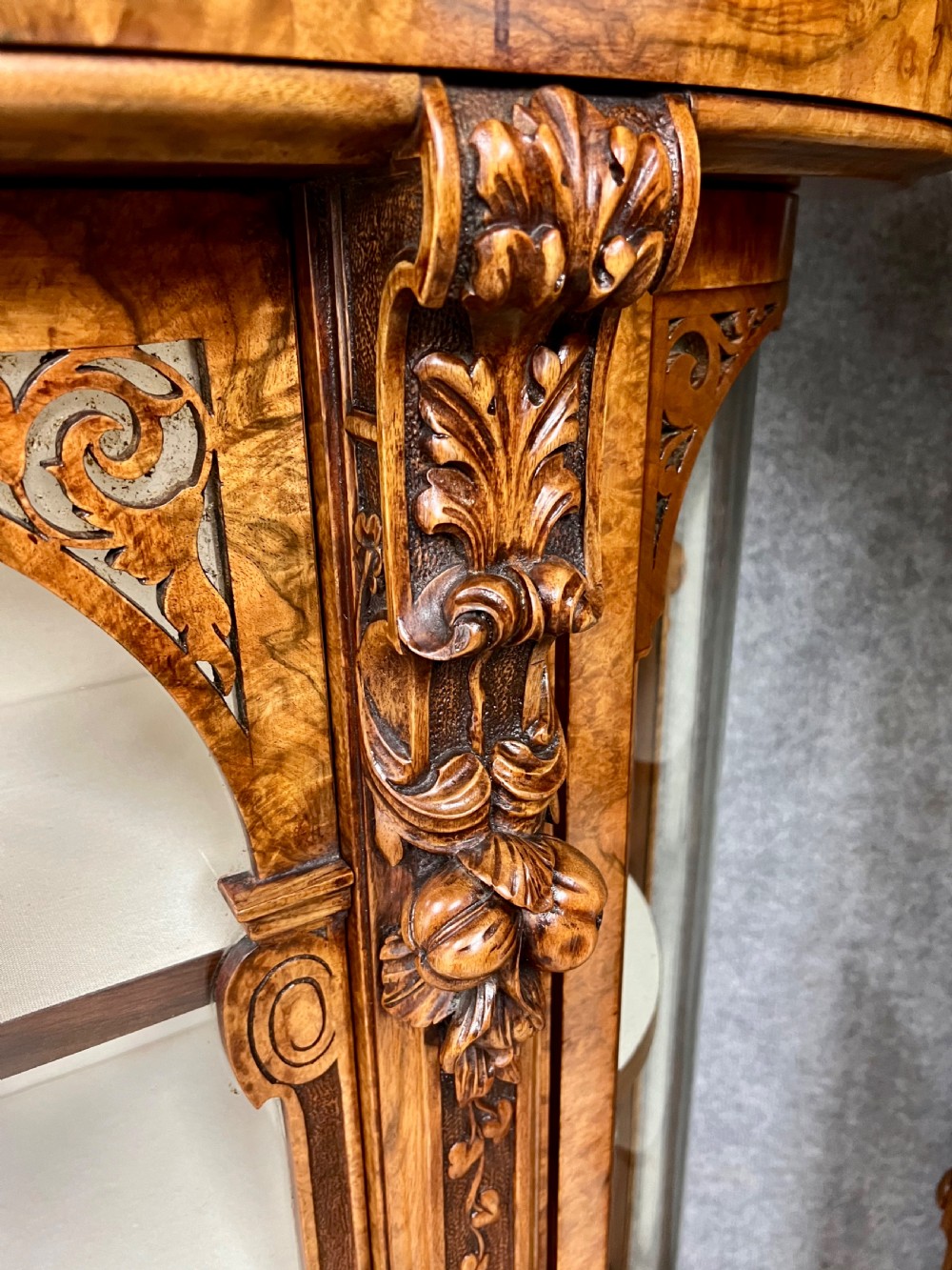 A pair of matching Victorian burr walnut cabinets featuring carved foliate detailing, open central shelving, and curved glass side compartments. View IV