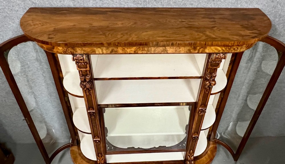 A pair of matching Victorian burr walnut cabinets featuring carved foliate detailing, open central shelving, and curved glass side compartments. View VII