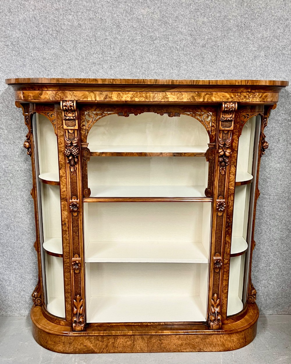 A pair of matching Victorian burr walnut cabinets featuring carved foliate detailing, open central shelving, and curved glass side compartments. View IX