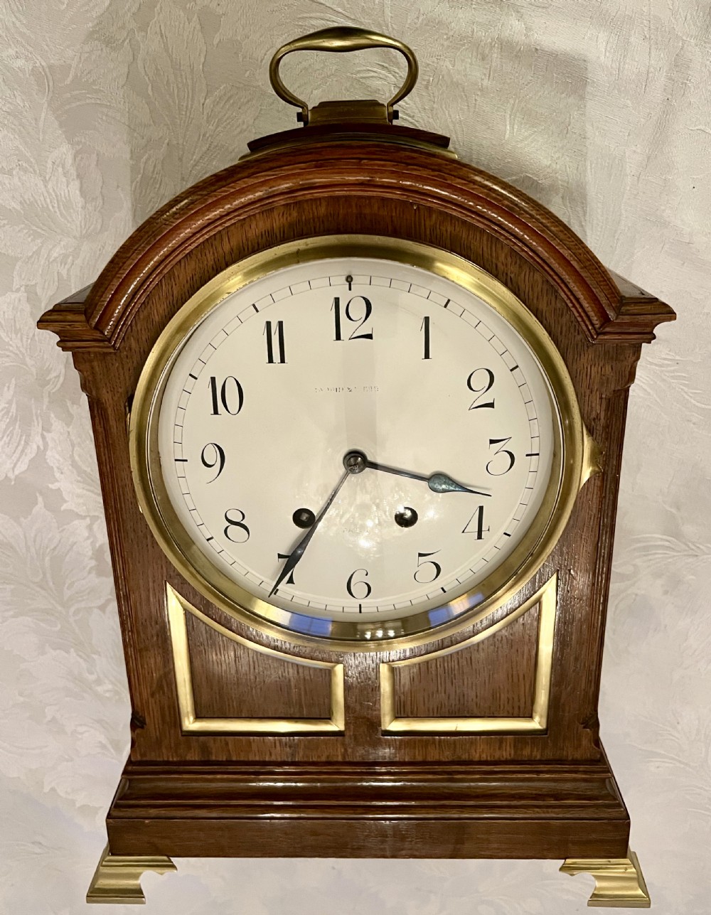 A Georgian style wooden bracket clock featuring an arched case, brass carrying handle, white dial with Arabic numerals, brass inlay, and bracket feet.