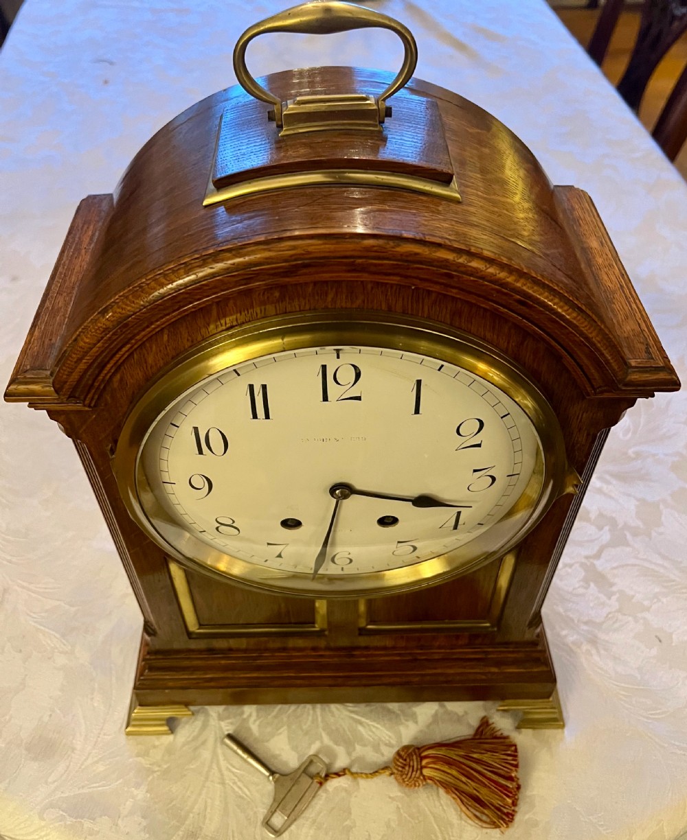 A Georgian style wooden bracket clock featuring an arched case, brass carrying handle, white dial with Arabic numerals, brass inlay, and bracket feet. View II