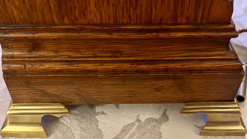 A Georgian style wooden bracket clock featuring an arched case, brass carrying handle, white dial with Arabic numerals, brass inlay, and bracket feet. View VII
