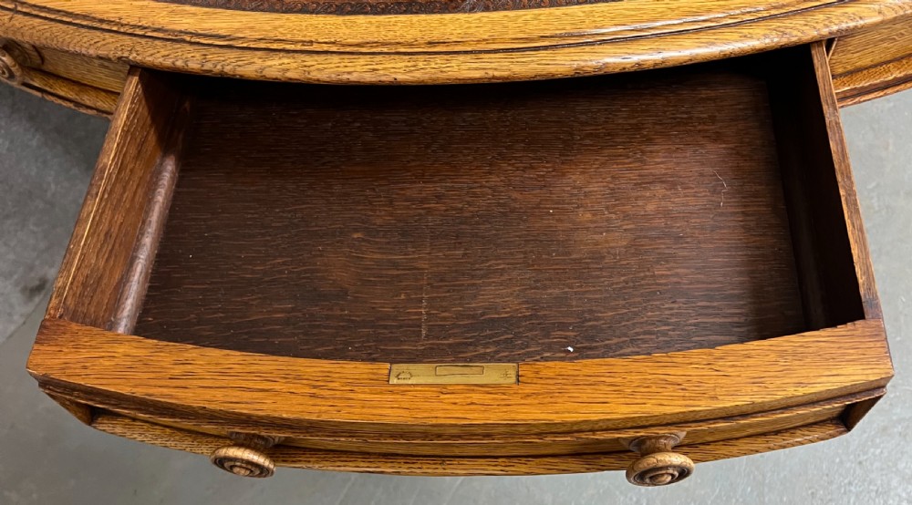 An antique Victorian oval oak library table featuring a leather inset top, perimeter frieze drawers, and a heavy carved pedestal base with scrolled legs on castors. View IV