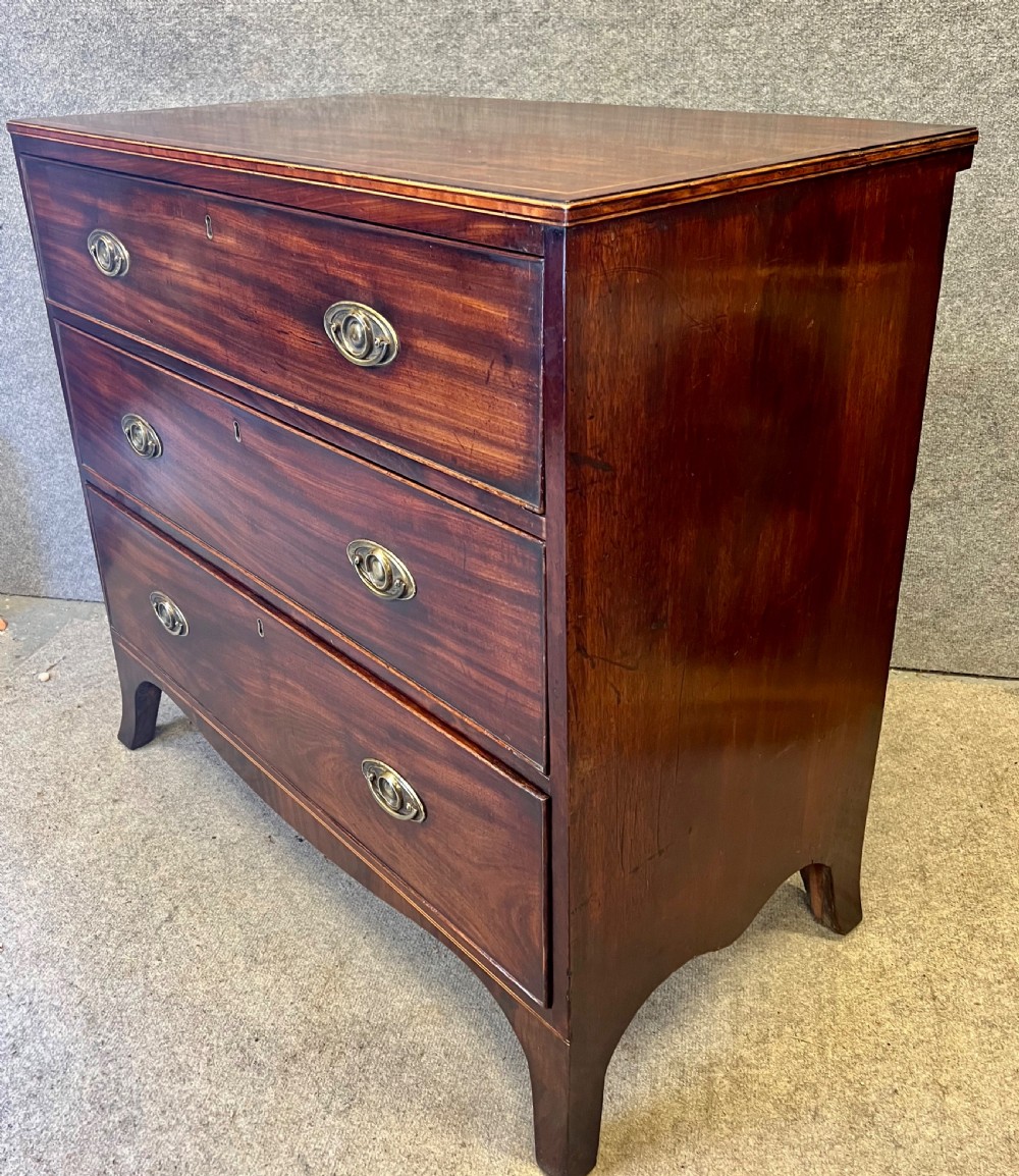 A George III mahogany chest of drawers featuring three graduated drawers with brass oval handles and line inlay on shaped bracket feet. View III