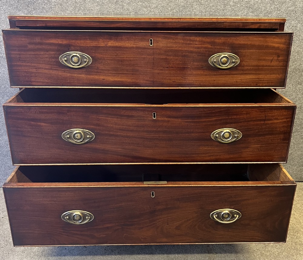 A George III mahogany chest of drawers featuring three graduated drawers with brass oval handles and line inlay on shaped bracket feet. View VIII