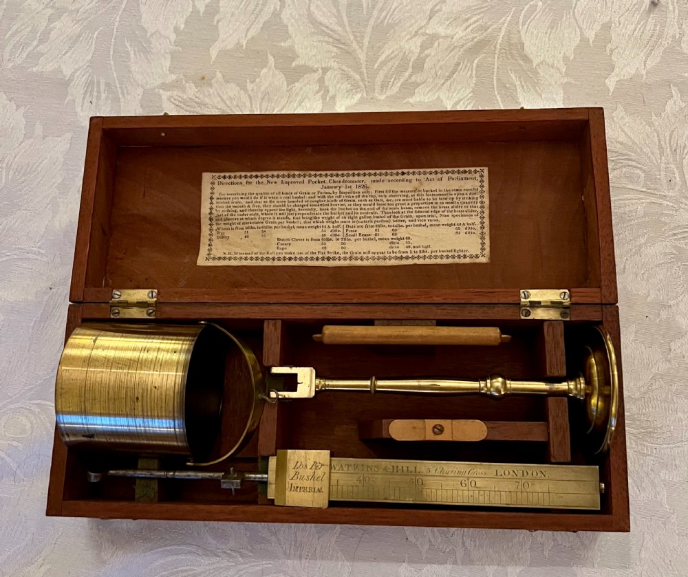 An open mahogany case containing a brass chondrometer grain scale with its balance beam, measuring bucket, and original instructional label on the inner lid.