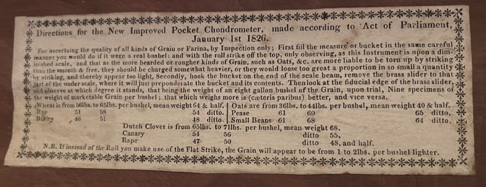 An open mahogany case containing a brass chondrometer grain scale with its balance beam, measuring bucket, and original instructional label on the inner lid. View II