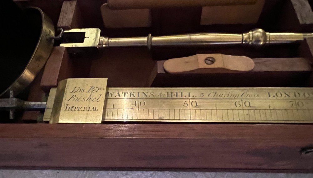 An open mahogany case containing a brass chondrometer grain scale with its balance beam, measuring bucket, and original instructional label on the inner lid. View III