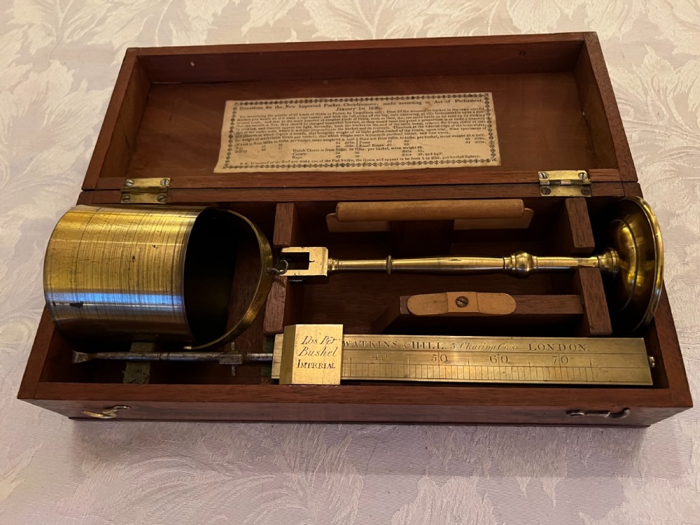 An open mahogany case containing a brass chondrometer grain scale with its balance beam, measuring bucket, and original instructional label on the inner lid. View VI