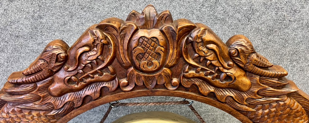 A hand-carved dark wood circular gong stand featuring twin dragon motifs and claw feet, suspending a central brass gong with a red textile mallet below. View III