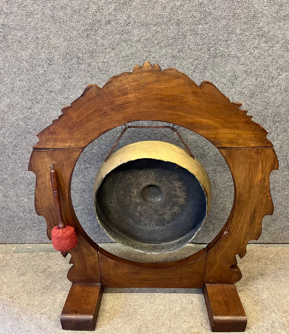 A hand-carved dark wood circular gong stand featuring twin dragon motifs and claw feet, suspending a central brass gong with a red textile mallet below. View VI