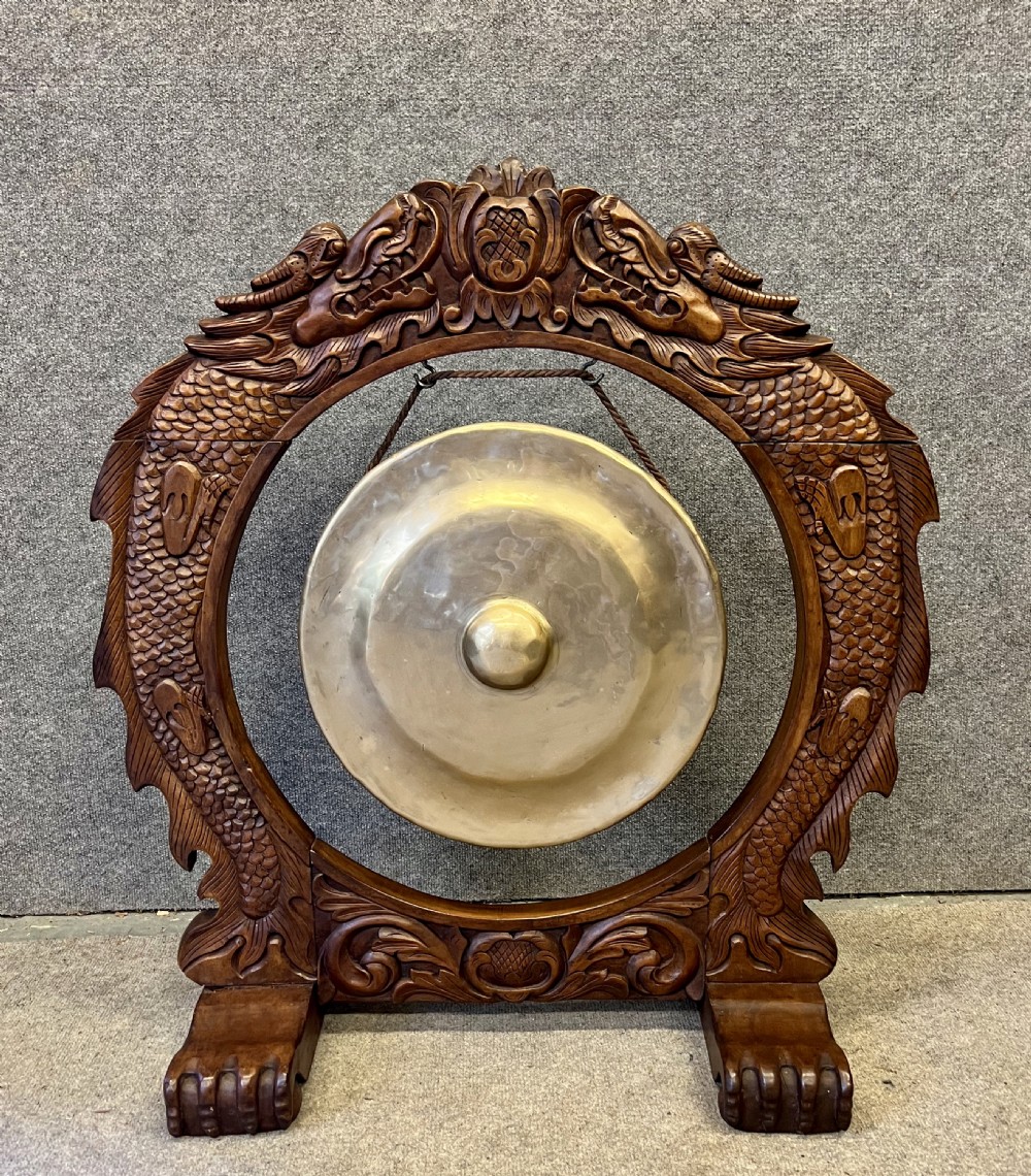 A hand-carved dark wood circular gong stand featuring twin dragon motifs and claw feet, suspending a central brass gong with a red textile mallet below. View VIII
