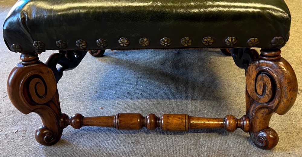 A long, low carved walnut stool featuring dark green leather upholstery secured with decorative brass studs along the apron. View VII