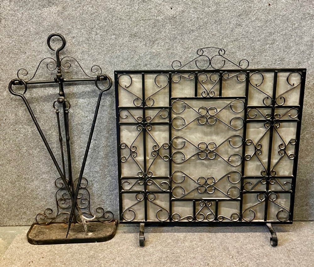 A wrought iron fire screen featuring decorative scrollwork alongside a matching companion set stand with fire tools.