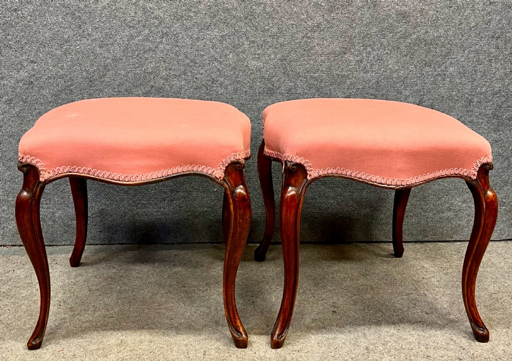 A pair of Victorian footstools with pink upholstered seats, decorative braided gimp trim, and carved dark wood cabriole legs. View III