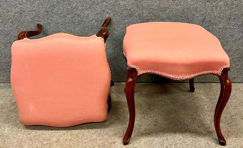 A pair of Victorian footstools with pink upholstered seats, decorative braided gimp trim, and carved dark wood cabriole legs. View IV