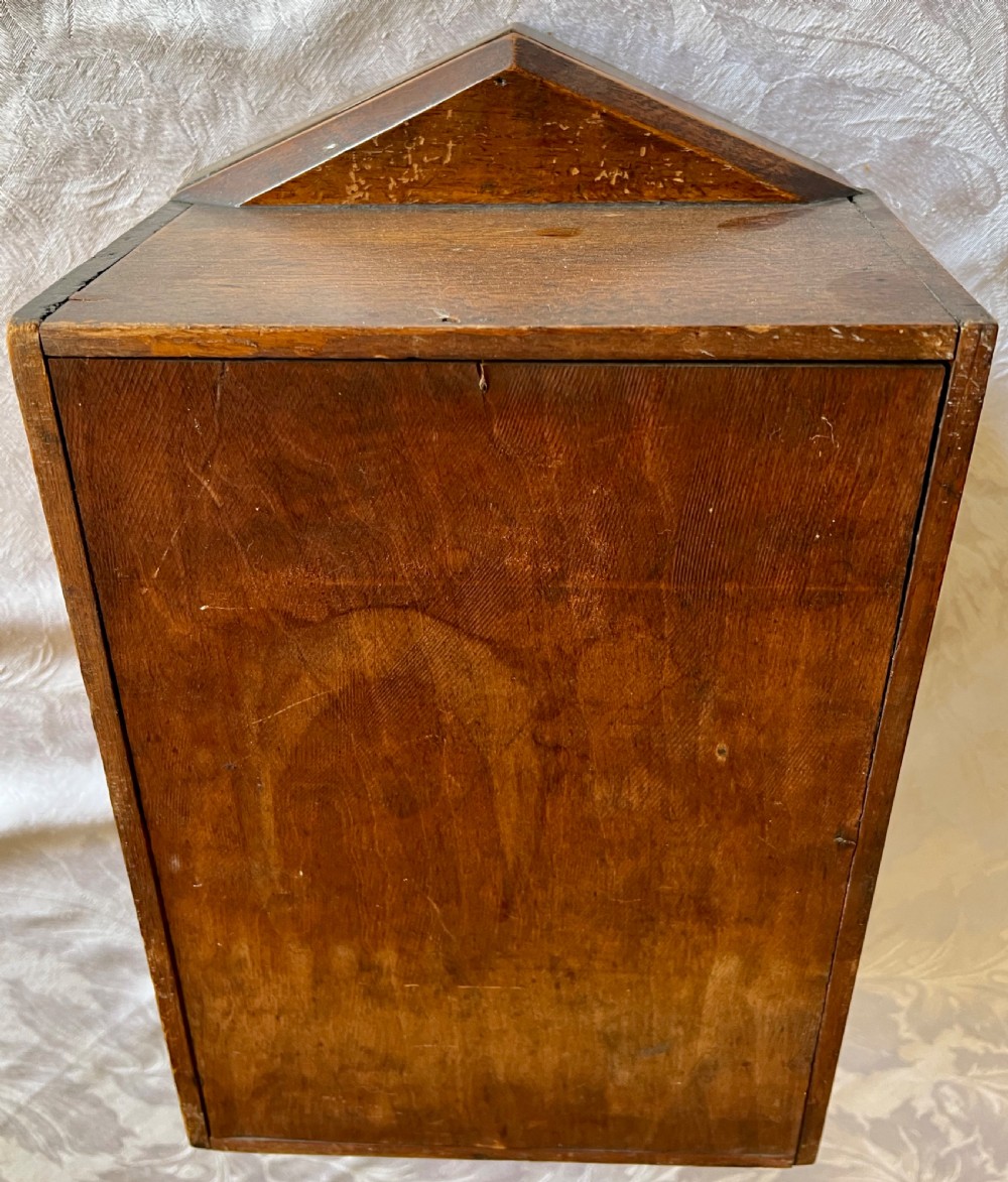 A wall-mounted carved oak letter box with a pointed top, horizontal aperture slot, side metal catch, and carved emblems on the front panel. View VII