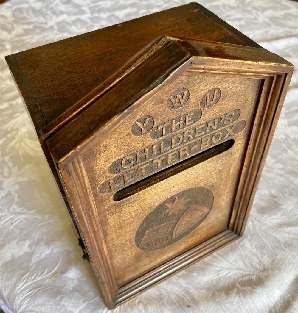 A wall-mounted carved oak letter box with a pointed top, horizontal aperture slot, side metal catch, and carved emblems on the front panel. View VIII