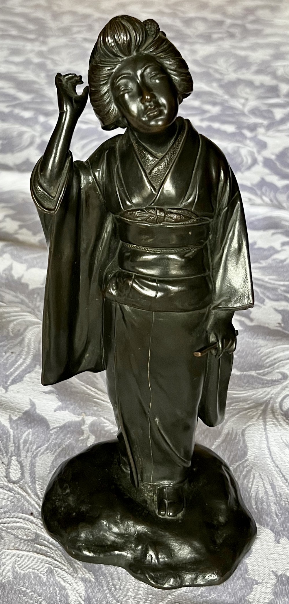 A dark patinated bronze figure depicting a Japanese woman in a traditional kimono with an intricate hair arrangement on an integral base.
