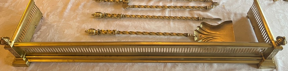 A Victorian polished brass fireplace fender featuring integrated rail ends and a set of three matching barley twist brass fire irons including shovel, tongs, and poker. View III