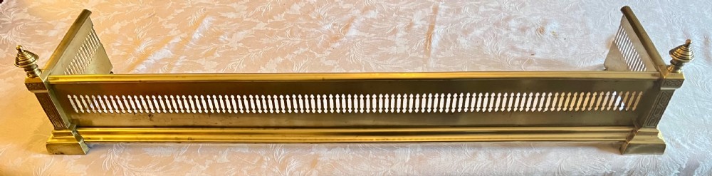 A Victorian polished brass fireplace fender featuring integrated rail ends and a set of three matching barley twist brass fire irons including shovel, tongs, and poker. View IV