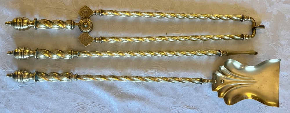 A Victorian polished brass fireplace fender featuring integrated rail ends and a set of three matching barley twist brass fire irons including shovel, tongs, and poker. View VII