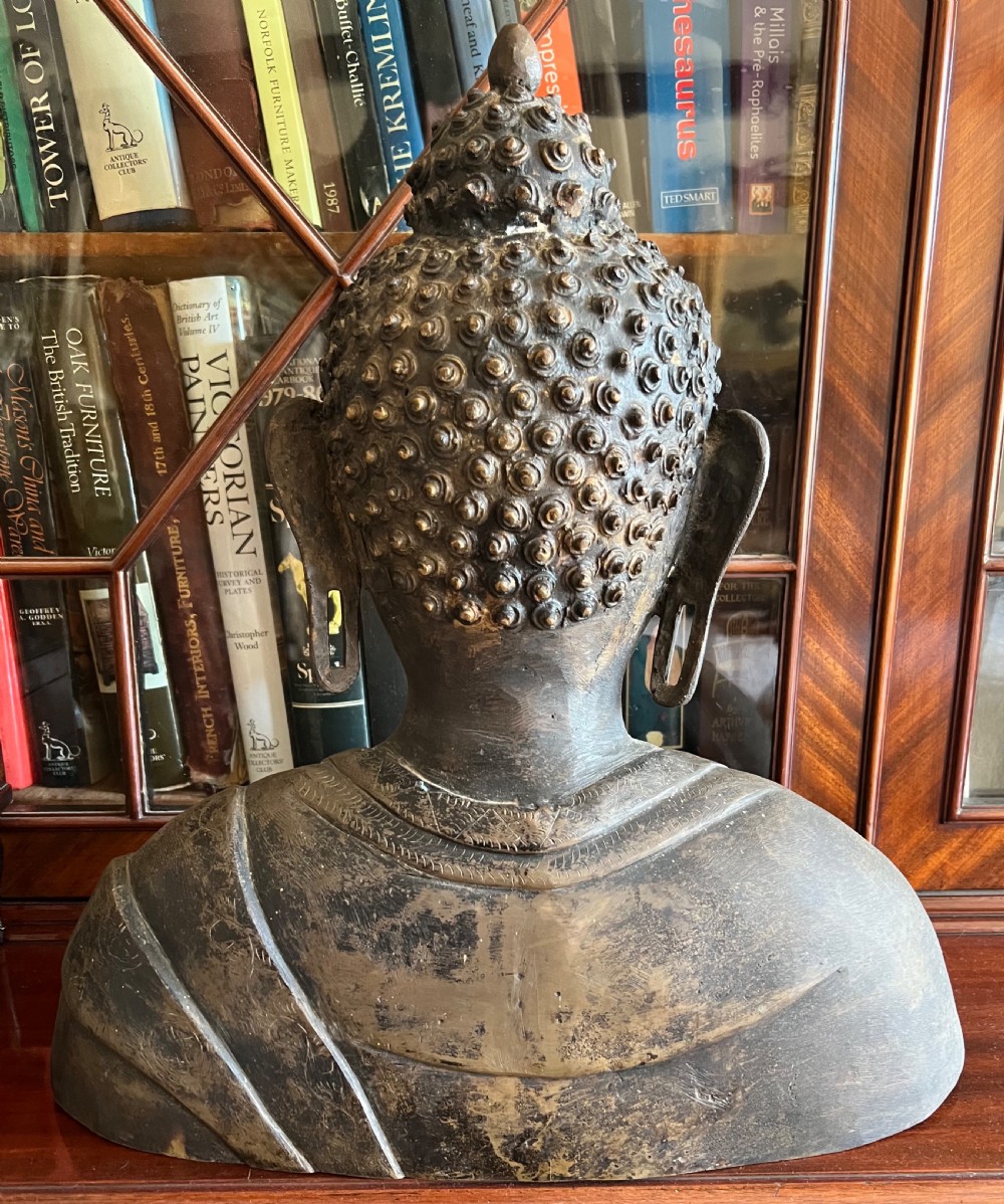 A cast bronze bust depicting a Buddha with downcast eyes, stylized hair curls, elongated earlobes, and draped robes. View II