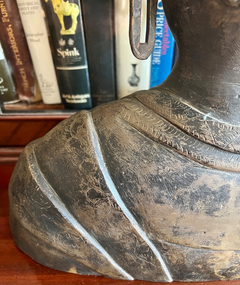 A cast bronze bust depicting a Buddha with downcast eyes, stylized hair curls, elongated earlobes, and draped robes. View VII